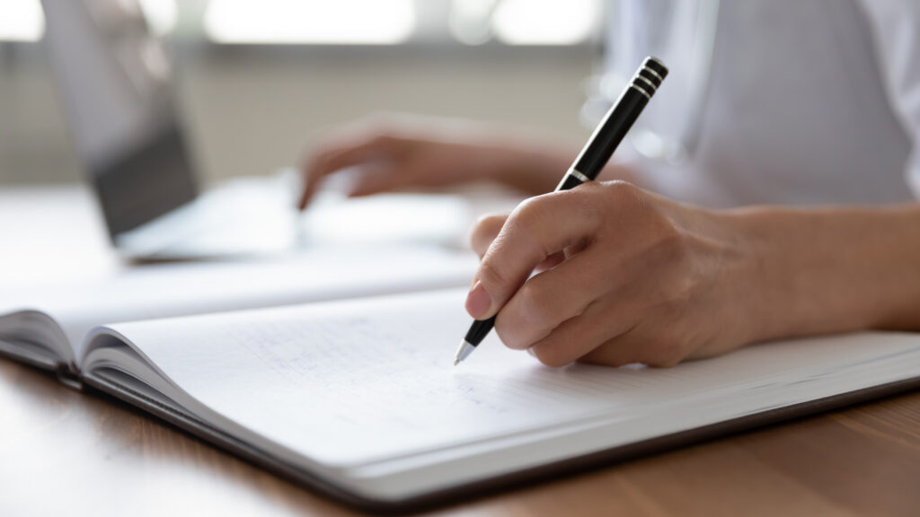 Picture of a hand writing in a book with a pen