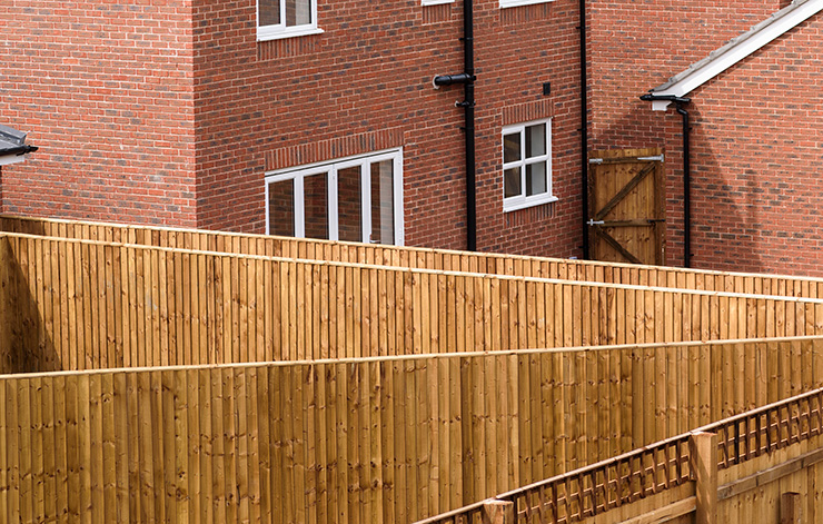 Picture of a wooden fence with red brick house behind it 