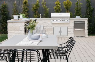 White stoned outdoor kitchen with sink and grill behind dining table