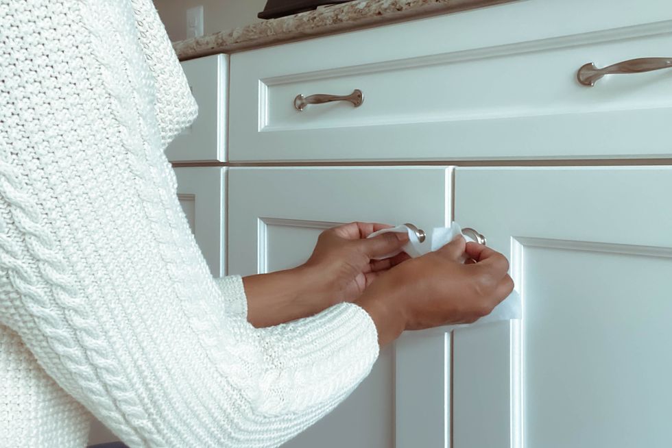 woman cleans cabinet hardware using disinfectant wipe