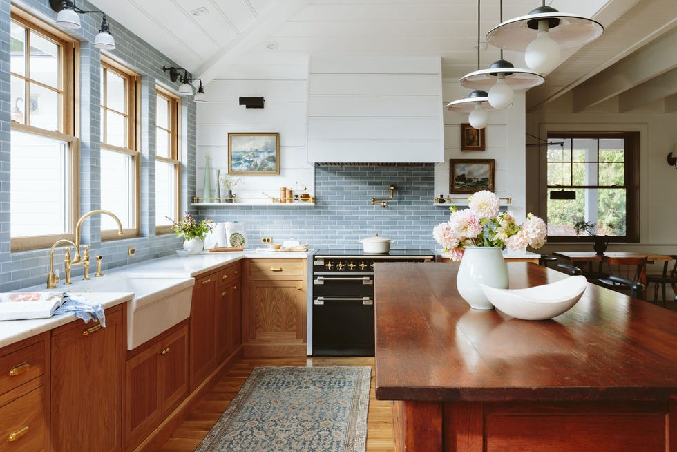 a well designed kitchen featuring wooden cabinets and a contrasting white countertop it includes a farmhouse sink and a modern stove with a sleek hood above it light blue tiles cover the wall space between the countertop and cabinets, adding a soft touch