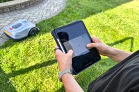 A person controls the Hookii Neomow X Pro Robotic Lawn Mower with a tablet