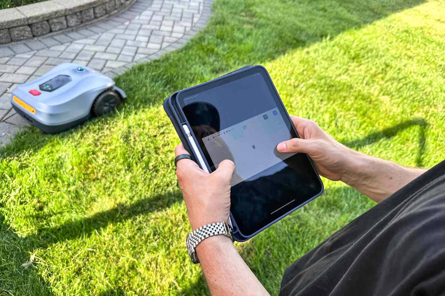 A person controls the Hookii Neomow X Pro Robotic Lawn Mower with a tablet